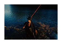 Man in a bucket hat with a fishing rod standing in a lake.
