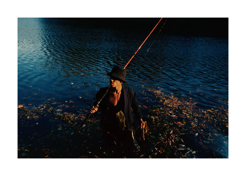 Man in a bucket hat with a fishing rod standing in a lake.