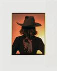 A woman with short hair and a cowboy hat dressed in a jacket with a cowboy print.