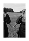 Two women dressed in black walking on a field and holding hands.