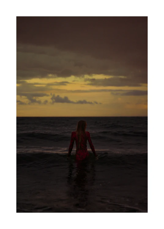A woman in a red dressing gown walking into the ocean during sunset.