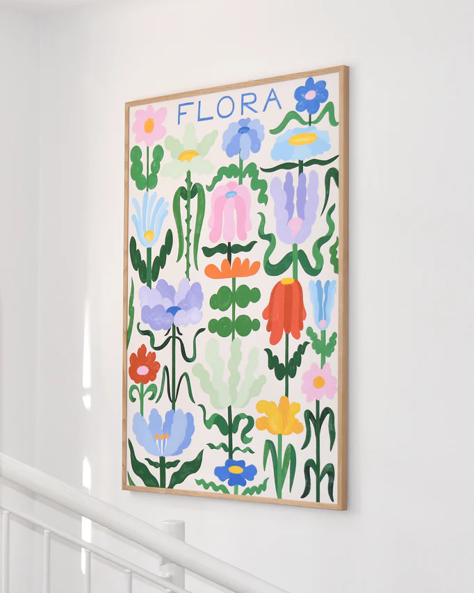 The Flora on White Poster showcases vibrant abstract flowers in various shapes and colors with elegant handwritten typography, hanging on a white wall above a staircase railing.