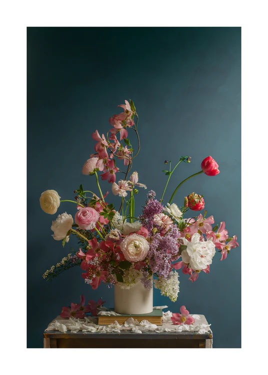 The Spring Ballet Poster showcases a floral arrangement with pink orchids, white ranunculus, lilac blooms, and a single red tulip in a white vase on wood, set against a blue background adorned with scattered petals.