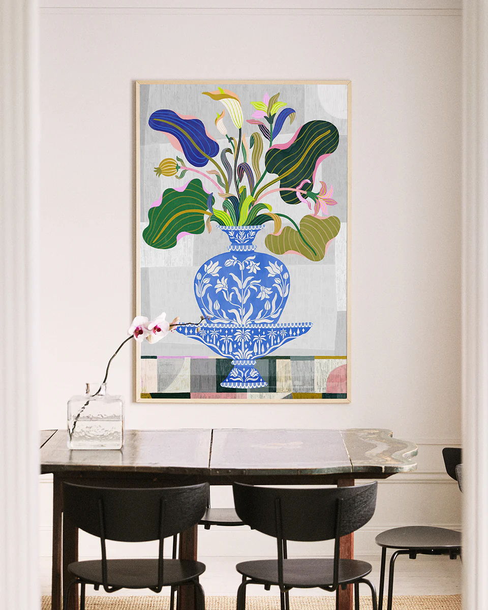 A dining room showcases a dark wooden table with black chairs, adorned with an orchid in a glass vase. A vibrant Vase Poster, inspired by Persian and Indian floral art, hangs on the light-colored wall, adding elegance.