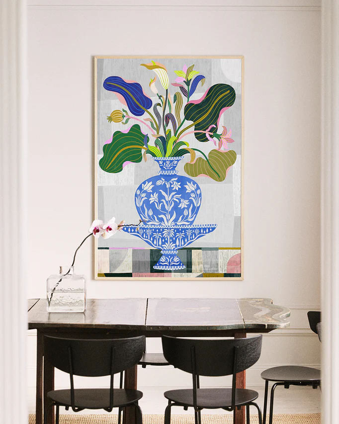 A dining room showcases a dark wooden table with black chairs, adorned with an orchid in a glass vase. A vibrant Vase Poster, inspired by Persian and Indian floral art, hangs on the light-colored wall, adding elegance.