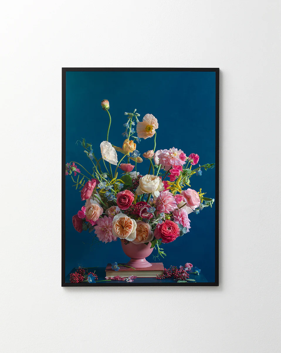 The Pink Kiss Poster features a framed artwork of a romantic bouquet with assorted flowers, including pink and white roses, set against a deep blue background. An elegant arrangement in a pink vase with some flowers spilling over the edge.