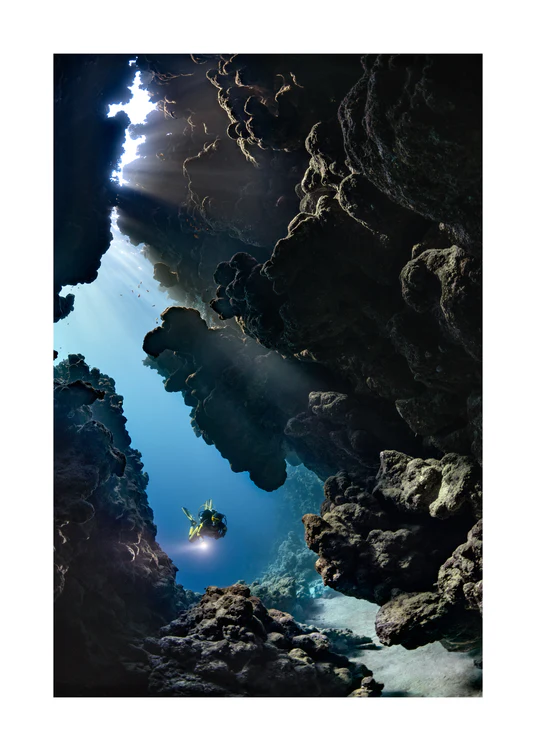 Diver swimming in the gap between cliff walls deep down in the ocean.