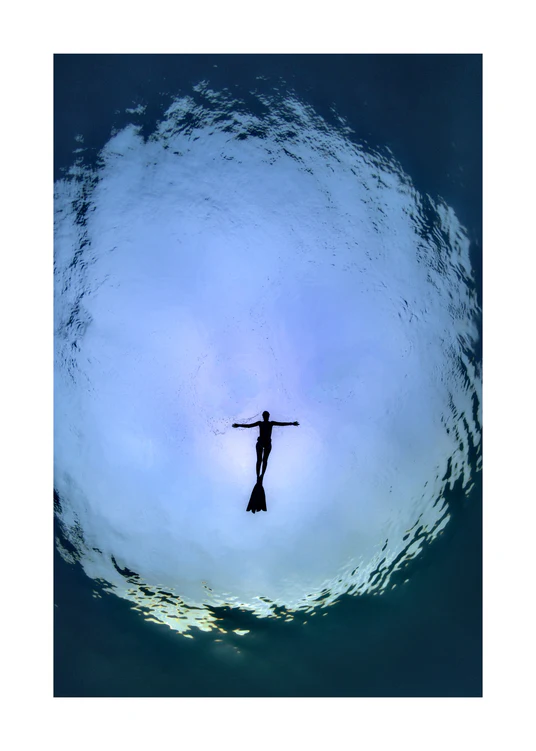 Diver floating underneath the surface of the sea captured from underneath.
