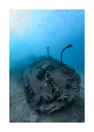 Shipwreck on the bottom of a deep blue ocean with a diver behind the wheel.