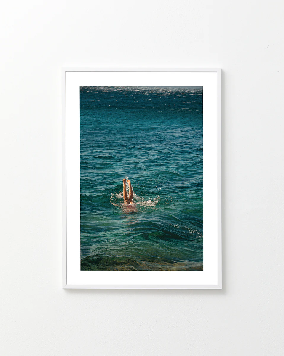 Legs of a person diving into the sea with their torso under the water’s surface.
