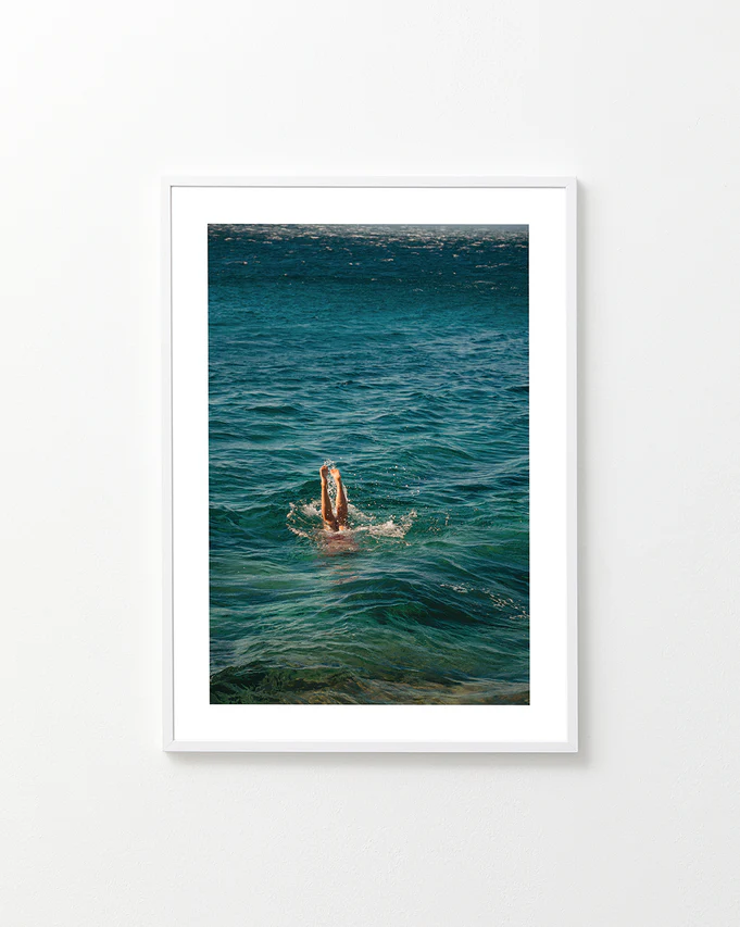 Legs of a person diving into the sea with their torso under the water’s surface.