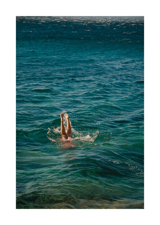 Legs of a person diving into the sea with their torso under the water’s surface.