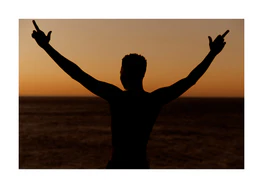 Man standing in front of a sea at sunset and flipping everybody off.