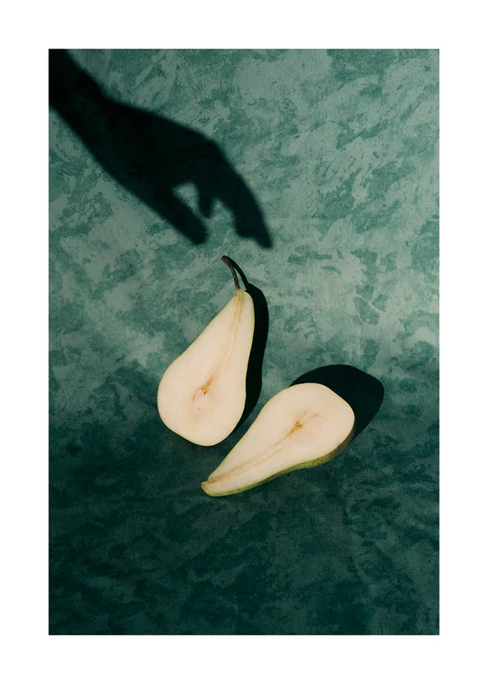Still life of a pear cut in half and a shadow of a hand reaching for it.