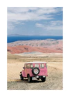 Pink jeep standing in a desert with pink sand dunes and an ocean in the horizon.
