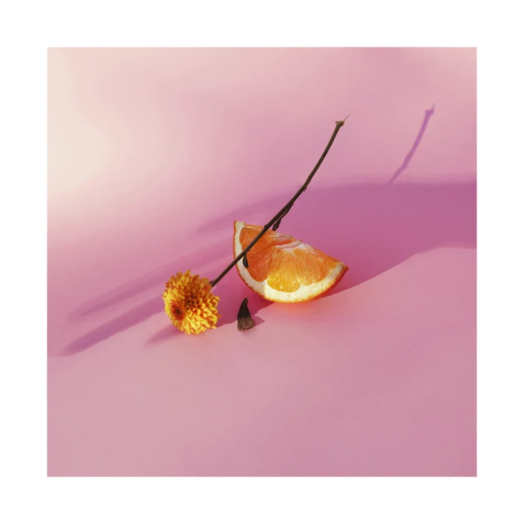 Stillebenporträtt av en apelsin och en blomma på en rosa yta.