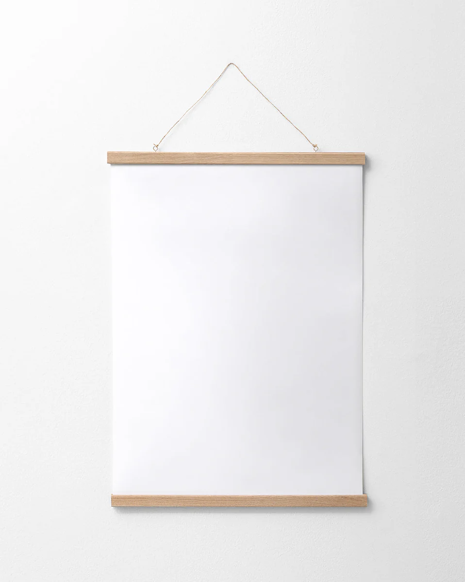 A blank white poster is elegantly displayed on a white wall, framed with the Poster hanger Oak at the top and bottom. It is suspended by a thin attached string, creating a seamless look that highlights its simple design.