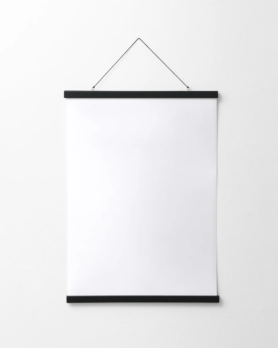 A blank white poster hangs on a plain white wall, elegantly secured by the Poster hanger Black, which features discreet magnets and two thin black bars for a sleek finish.