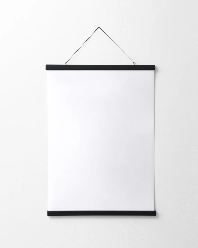 A blank white poster hangs on a plain white wall, elegantly secured by the Poster hanger Black, which features discreet magnets and two thin black bars for a sleek finish.