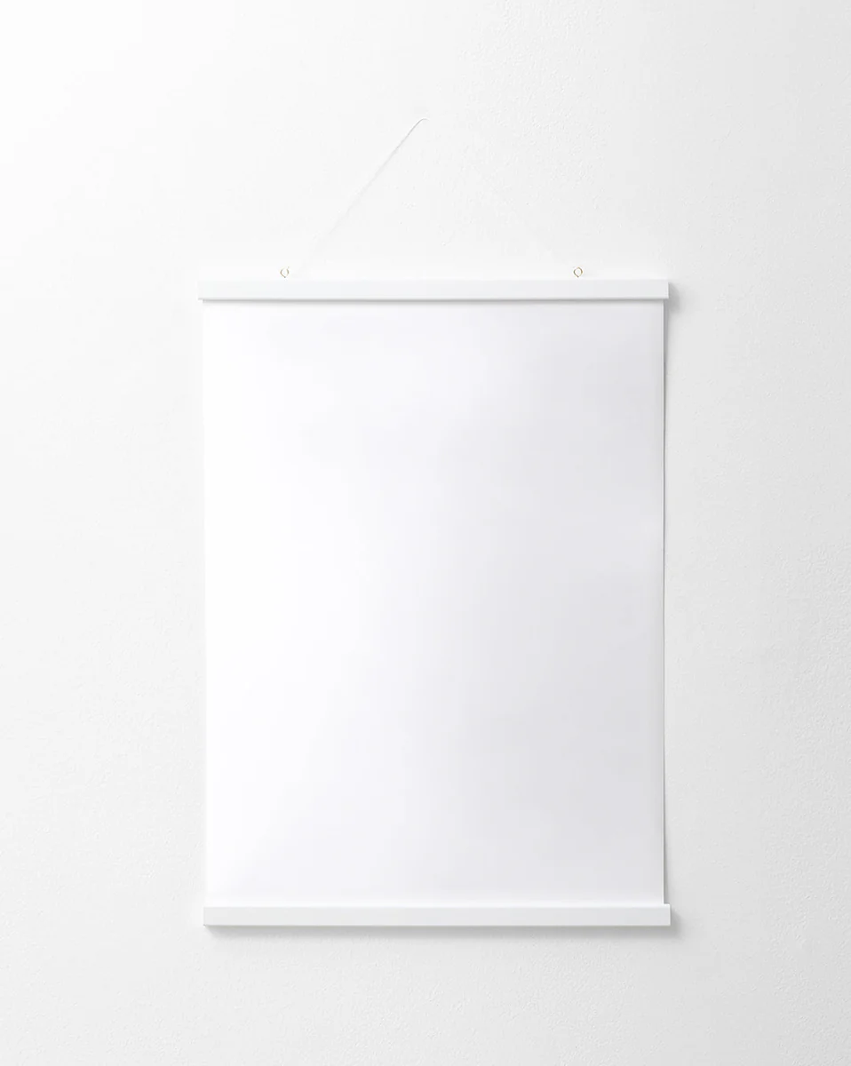 The Poster hanger White elegantly displays a blank white poster on a white wall. It features thin solid pine strips at the top and bottom, suspended by a string from two small nails, enhancing its minimalist charm.