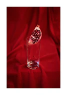 Slice of pomegranate in a glass standing on a blood red sheet.