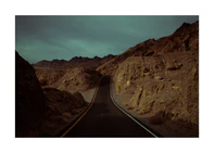 Asphalt road slithering its way through a rough mountain scenery.
