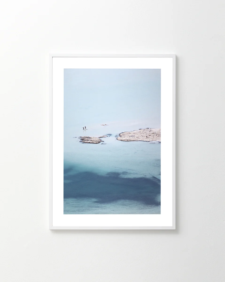 The Eavesdropping IX Poster showcases a serene aerial seascape with two people on a rocky outcrop in tranquil turquoise water. Soft waves and subtle color gradients create an inspiring, captivating scene.