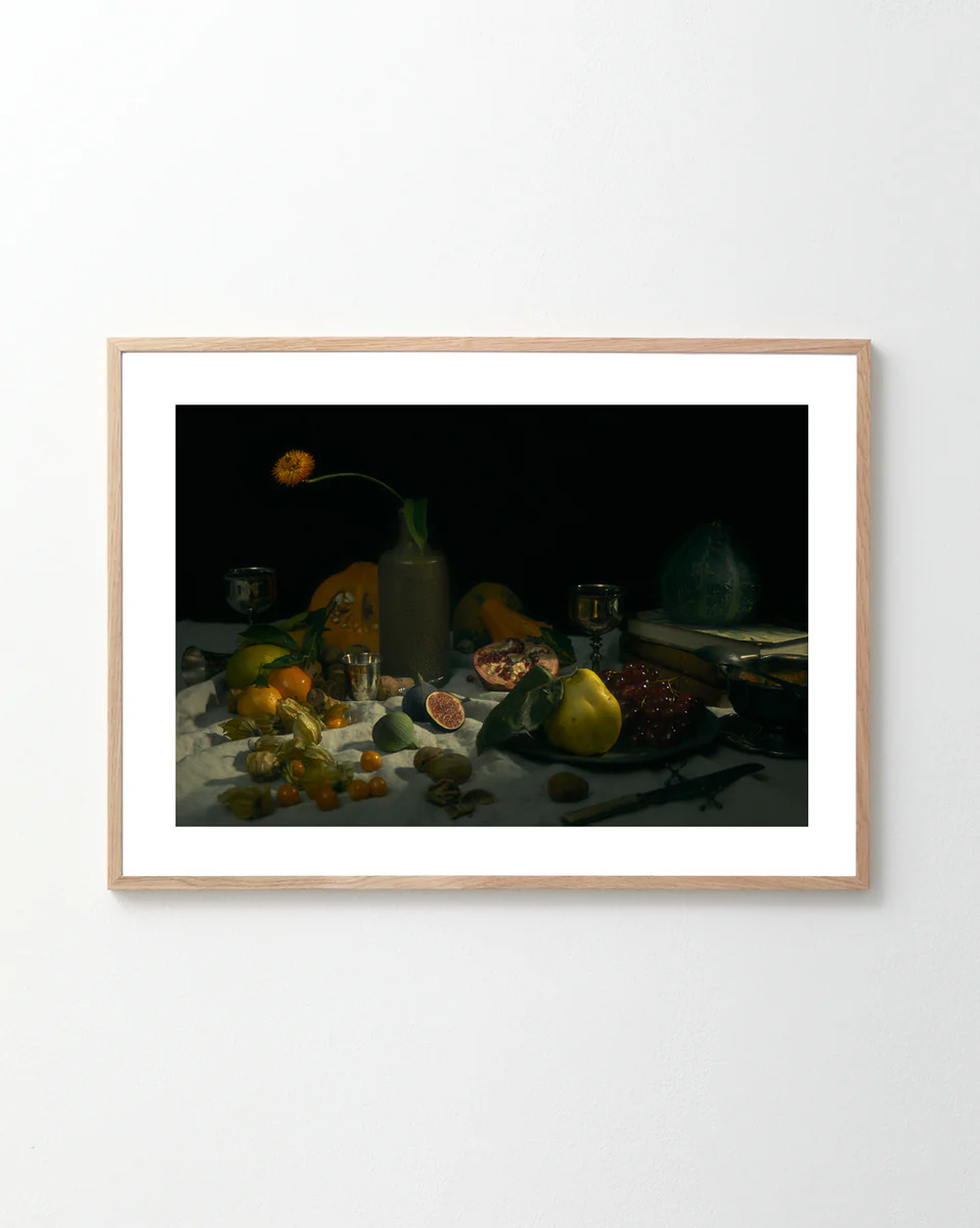 The Gloomy Picnic II Poster features a still life reminiscent of Paul Cézanne, displaying fruits like figs, pomegranate, and oranges alongside tableware against a dark background. A tall vase with a single flower adds to the dramatically illuminated composition, captured as if by a cameras eye.