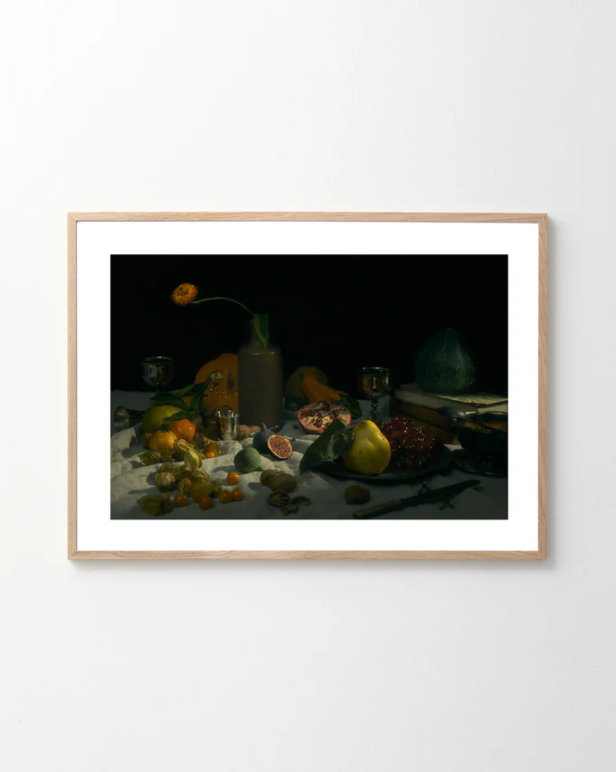 The Gloomy Picnic II Poster features a still life reminiscent of Paul Cézanne, displaying fruits like figs, pomegranate, and oranges alongside tableware against a dark background. A tall vase with a single flower adds to the dramatically illuminated composition, captured as if by a cameras eye.