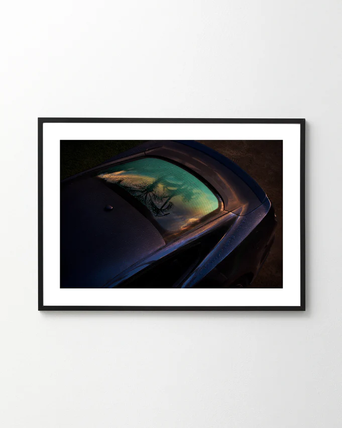 The Gas Up Poster captures a sleek car with dew on the windshield under a vibrant sky, embodying pedal to the metal. Displayed on a plain white wall and viewed from an elevated angle, it highlights dynamic presence.