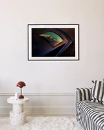 A modern living room boasts a striped sofa, a round white speckled side table with a brown lamp, and the Gas Up Poster, capturing the pedal to the metal spirit with car reflections of trees and sky on the cream-colored wall.