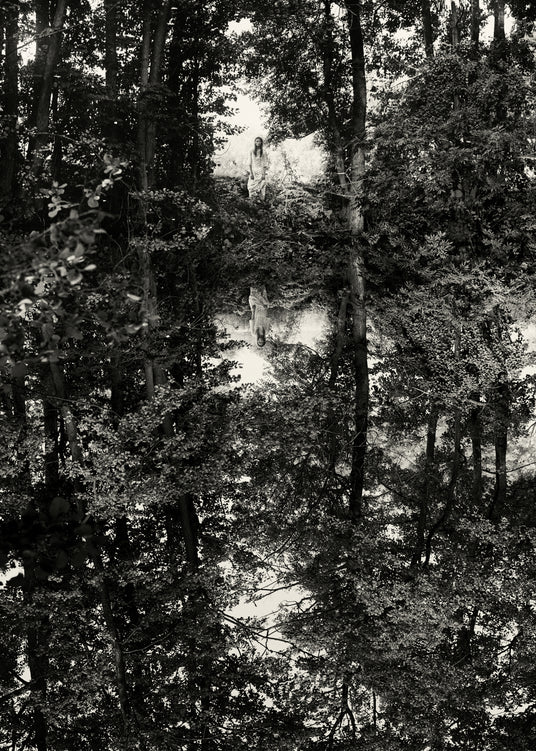 Woman standing in a forest reflected in the surface of a lake.