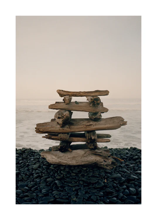 Sculpture made from driftwood standing on a black stone beach.